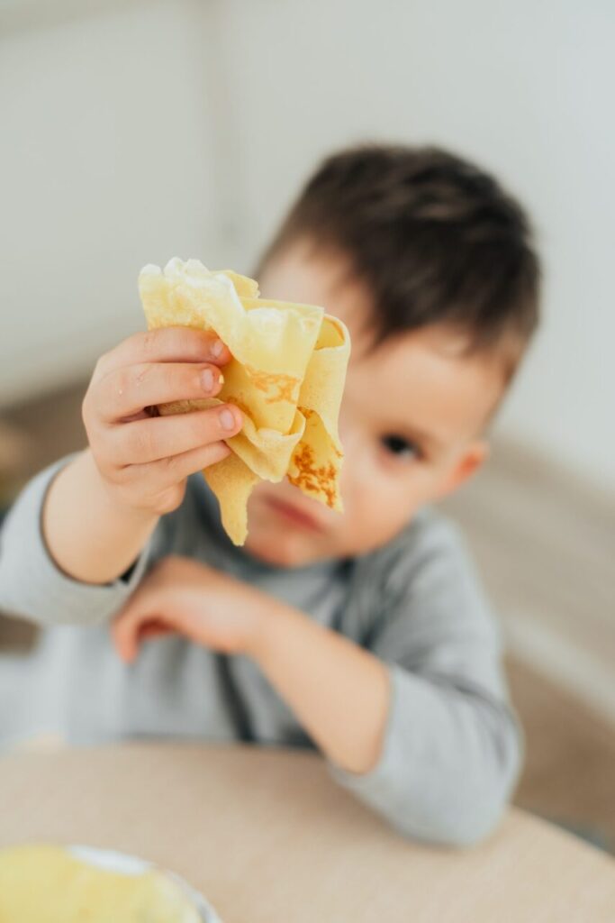 Enfant tenant et pressant un jouet Butter Squishy en forme de motte de beurre près d’un sapin de Noël.